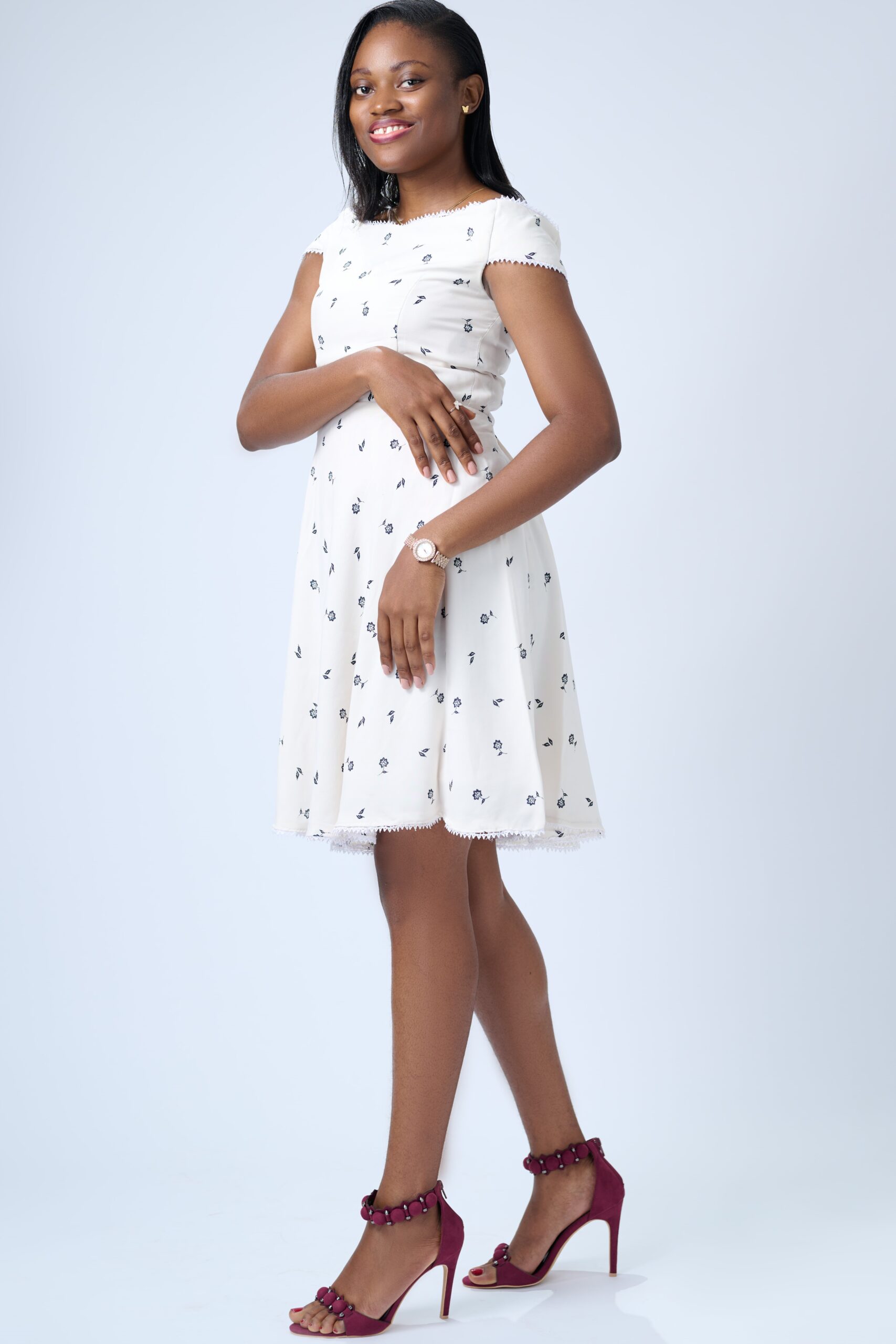 Picture of Jane OLUWADARE standing, slightly turned to the side, and with a bright smile. She is wearing a white dress and small gold butterfly earring studs. Her hair is down in a side part